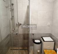 Shower corner and washing machine in the bathroom for a 2-room apartment with brown tiles.