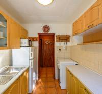 A kitchen in a cottage with wooden cabinets and appliances, warm tiles on the floor.