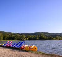 Pedal boats at the lake in Ružiná surrounded by greenery and hills under a blue sky.