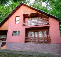 A wooden cottage in Ružiná, surrounded by greenery and with a terrace on the upper floor.