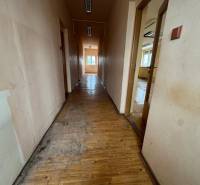 A hallway in a building with a wooden floor and rooms on both sides.
