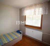A room in a 3-room apartment with a bed, a radiator, and a window with a white curtain.