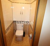 A toilet in a 3-room apartment with light tiles and storage space above the toilet.