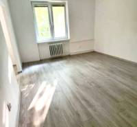 A bright room with a large window in a two-room apartment and wooden flooring.