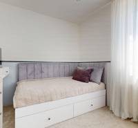 A bedroom in a family house with light furniture, a television, and curtains.