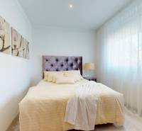 A bedroom in a family house with a light-colored bed, decorations, and a large window.
