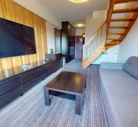 Living room in a 2-room apartment with a staircase and a television on a wooden wall.