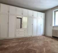 A room of a three-room apartment with a white built-in wardrobe and wooden flooring.