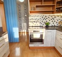 A kitchen in a studio apartment with wooden cabinets and mosaic tiles on the wall.