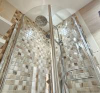 Modern shower cabin with mosaic tiles and shelves in a studio apartment.
