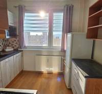 A kitchen in a studio apartment with wooden cabinets, tiles, and a window letting in light.
