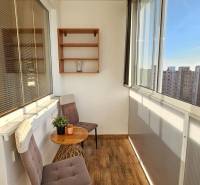 Glazed loggia with wooden flooring, chairs, and a view of the housing estate in a 1-room apartment.