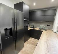 A kitchen in a 3-room apartment with black appliances and wooden flooring.