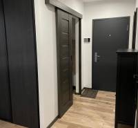 Entrance hallway to a 3-room apartment with wooden floors and dark sliding doors.