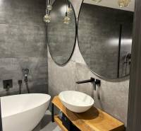 A bathroom in a 3-room apartment with stylish mirrors, a bathtub, and a wooden washbasin counter.