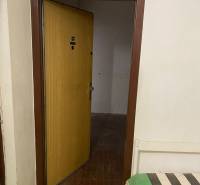 Open door in a 3-room apartment with a tiled floor and a bench with a colorful throw.