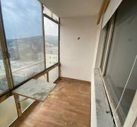 A glazed balcony of a 3-room apartment with a wooden floor and a view of the rooftops of buildings.