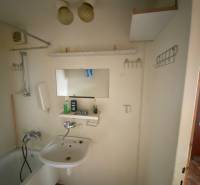 A bathroom with a bathtub and a sink in a 3-room apartment with storage shelves.