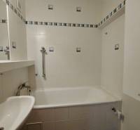 A bathroom with a bathtub, white tiles, and handrails in a 3-room apartment.