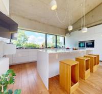 A kitchen in a family house with a wooden floor, bar stools, and large windows.