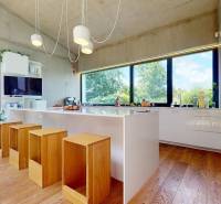 A kitchen in a family house with large windows, wooden floor, and white cabinets.