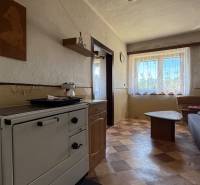 The interior of a family house with a kitchen stove, a sofa, and a table, with light entering through the window.