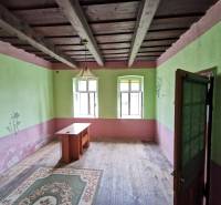 A room in a family house with a wooden ceiling, an old table, and a carpet.