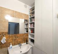 A bathroom in a 3-room apartment with a white sink, mirror, and storage cabinets.