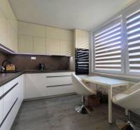 A kitchen in a 3-room apartment with seating and a large window with blinds.