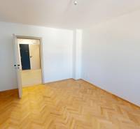 A room in a 2-room apartment with a parquet floor and white walls.
