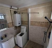 A bathroom in a 2-room apartment with a shower, washing machine, sink, and boiler.