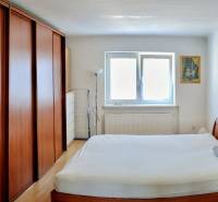 A bedroom with a wooden bed and wardrobe in a 2-room apartment, complemented by a window and a painting.