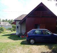 A car parked near the cottage in Klížska Nemá, surrounded by green lawn and trees.