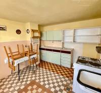 A kitchen in a family house, with an older stove and chairs on the table.