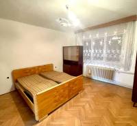Interior of a family house with wooden flooring, a bed, and curtains on the window.