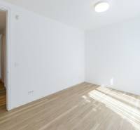 An empty room in a 3-room apartment with wood-patterned flooring and white walls.
