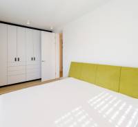 A bedroom with a white built-in wardrobe, a green headboard, and a wood-patterned floor.