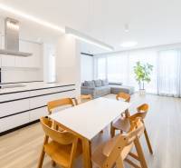 Bright living room with a dining table, kitchen, and wood-patterned flooring.