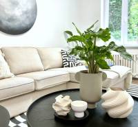 Bright living room corner with a sofa, a plant on a black table, geometric accessories.