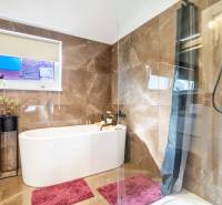 A bathroom in a family house with a bathtub, marble tiles, and pink carpets.