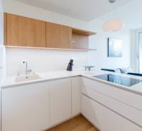 A kitchen in a 2-room apartment with white cabinets, wooden elements, and a large window.