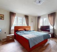 A bedroom in a family house with an orange bed, an armchair, and a television.