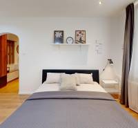 Bedroom in a one-room apartment with a bed, nightstand, and open access to the hallway.