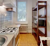 Kitchen in a studio apartment with a stove, sink, and wooden shelf.