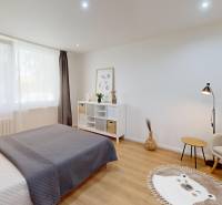 A bedroom in a studio apartment with a bed, an armchair, a carpet, and a window with dark curtains.