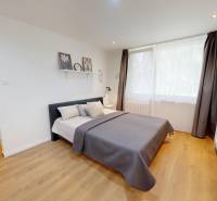 A simple bedroom with a gray bed, light accessories, and wooden flooring in a studio apartment.