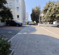 A paved path in Novalja leads to a 2-bedroom apartment, surrounded by trees and buildings.