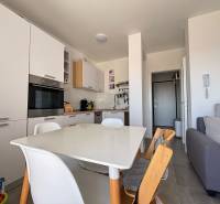 A kitchen in a 2-room apartment with white appliances and a wooden dining table.