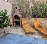 Garden space of a 2-bedroom apartment in Novalja with sunbeds and a grill surrounded by greenery.