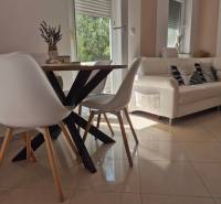 Interior of a 2-room apartment with a wooden table, white chairs, and a comfortable couch.